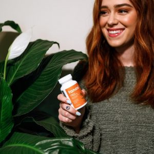 Woman with red hair in green shirt holding Tanasi CBD capsules