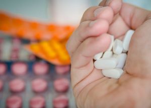 hand holding white pills with pink and orange pills in background
