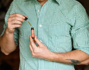Man in green shirt holding Tanasi CBD tincture and dropper